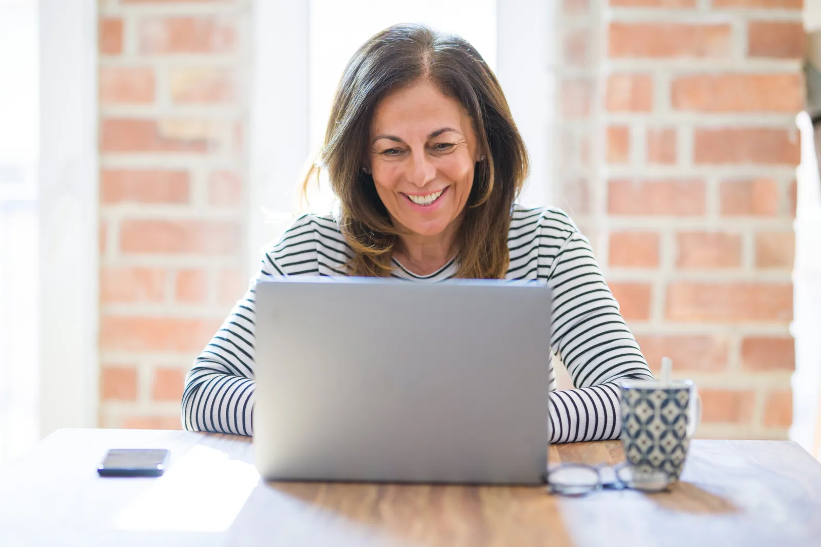 An adult learner smiling while studying online with a laptop