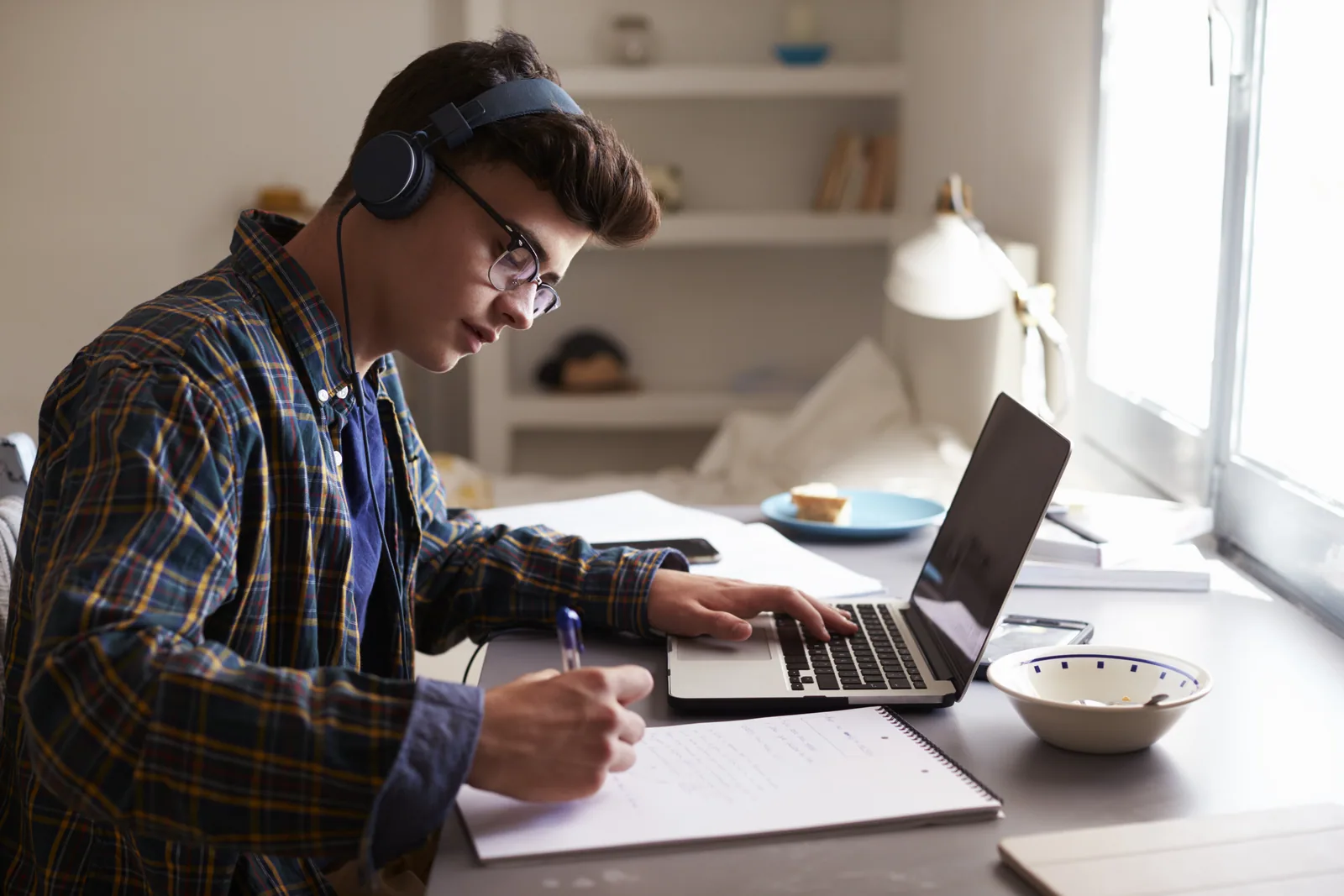 A teenage student wearing headphones while studying at a desk