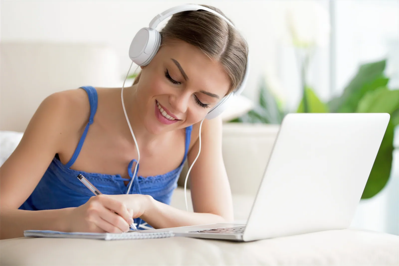 A student wearing headphones and taking notes during an online course