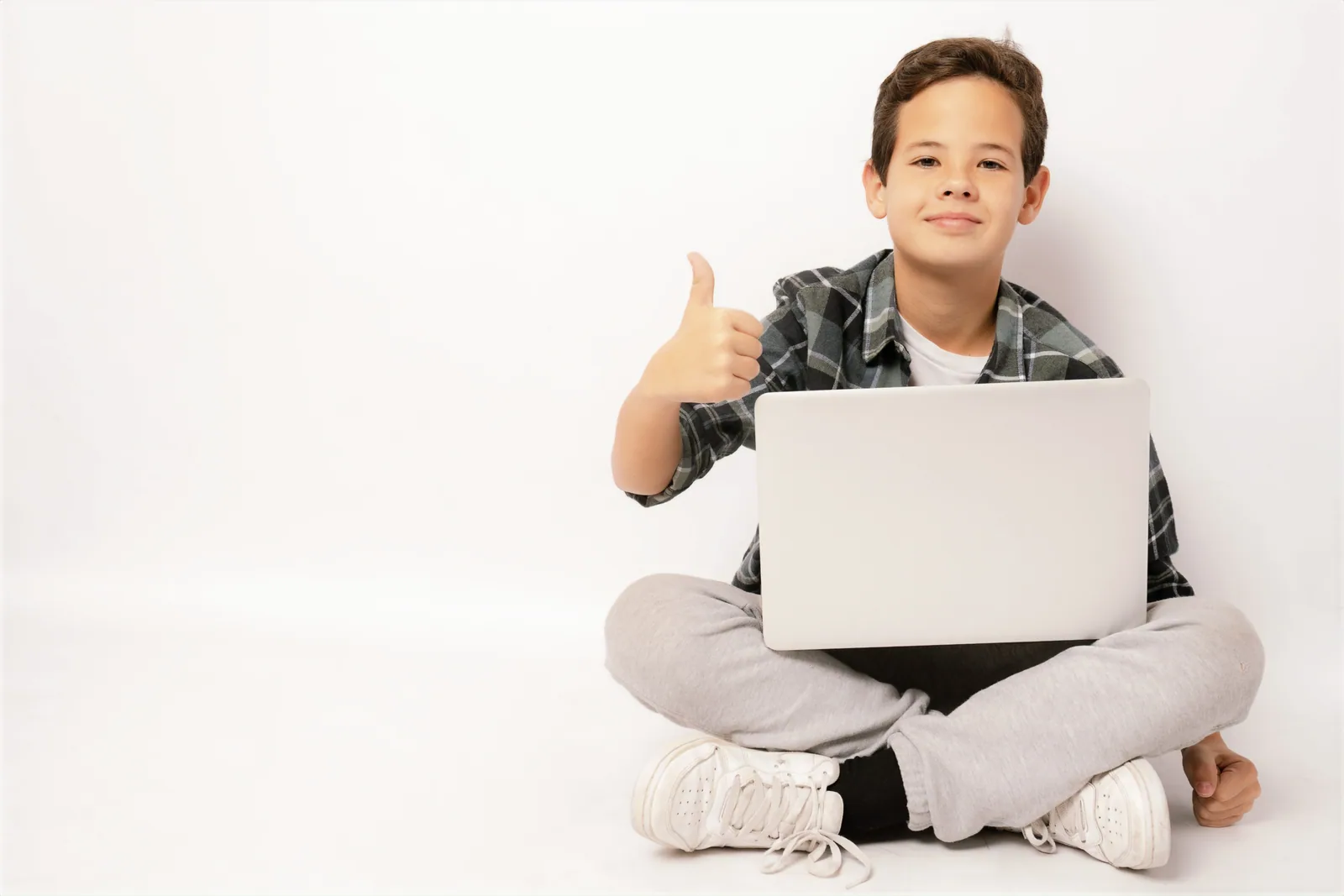 A child sitting with a laptop and giving a thumbs up